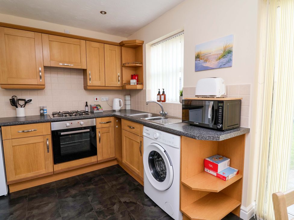 A kitchen with cabinets, oven, microwave, and washing machine at The Beach Escape in Prestatyn