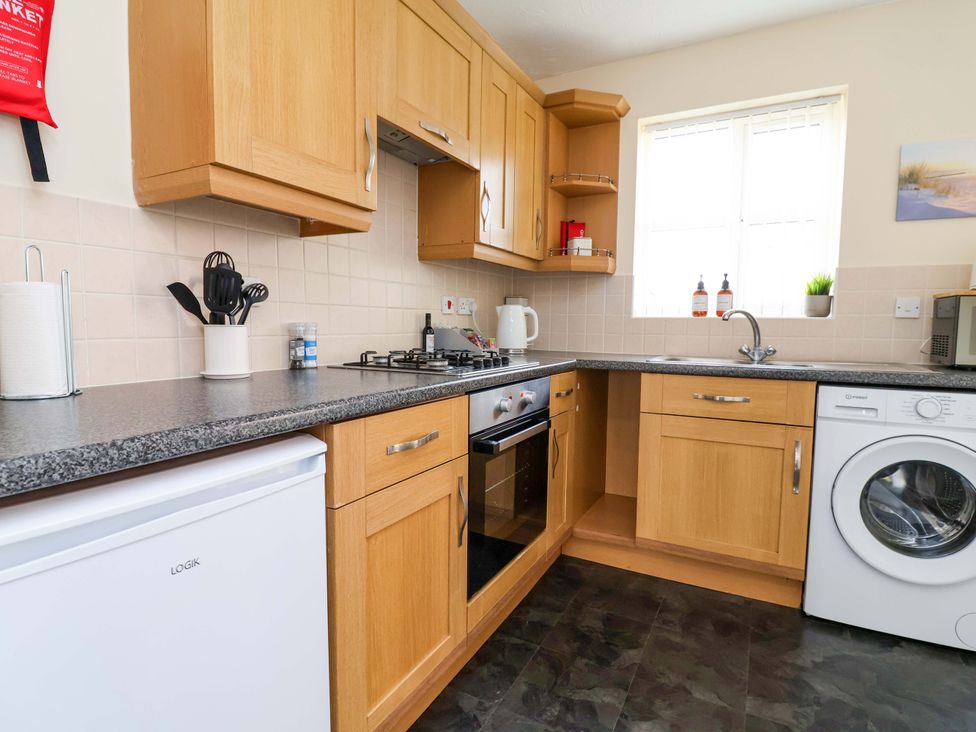 A kitchen with cabinets, sink, stove, and washing machine at The Beach Escape in Prestatyn