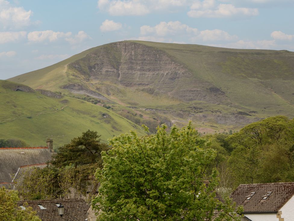 A mountain with greenery and rooftops in the foreground at The Toll Bar in Hope Valley