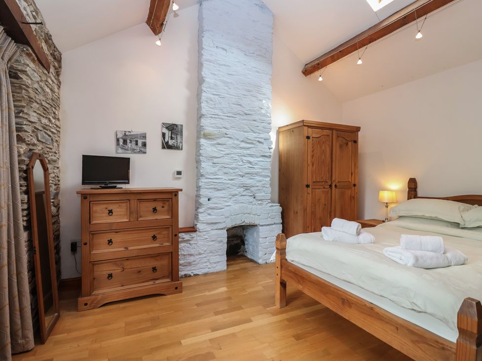 A bedroom with a bed, dresser, mirror and television at The Coach House in Tavistock