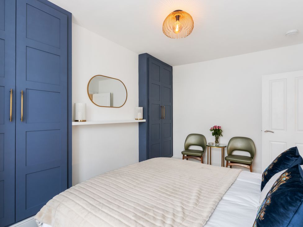 A bedroom with a bed, wardrobe, chairs and a mirror at The Sundial in St Austell