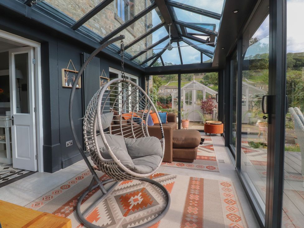 A conservatory with a hanging chair and sofa at Langcliffe House, Kettlewell