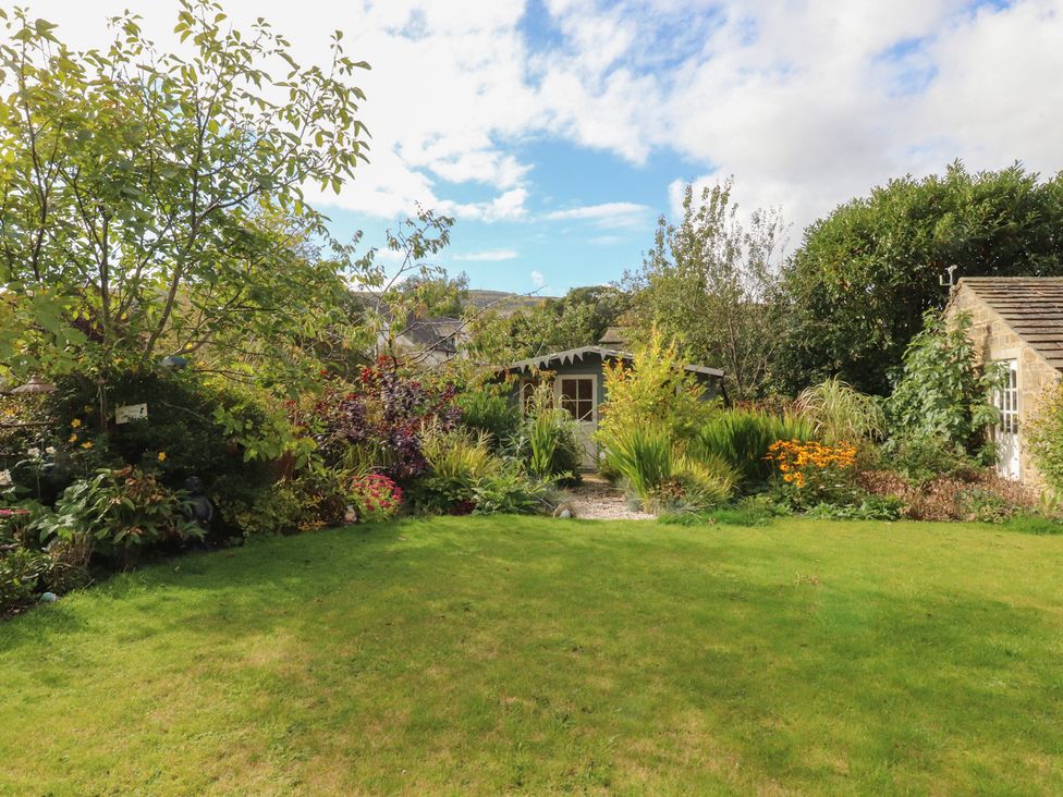A garden with grass, trees, flowers, and a shed at Langcliffe House in Kettlewell