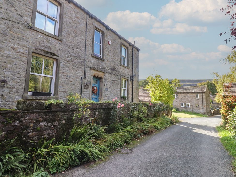 A stone house with a blue door and garden at Langcliffe House in Kettlewell