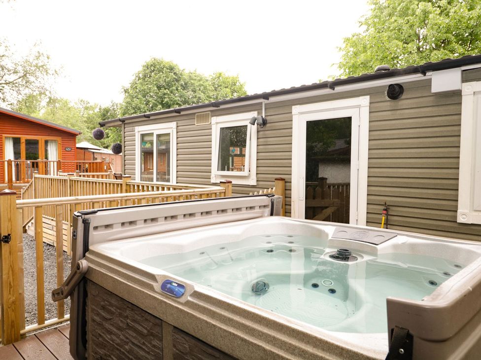 An outdoor area with a hot tub and wooden cabins at Owls Nook Lodge in Langdale 9, White Cross Bay near Windermere