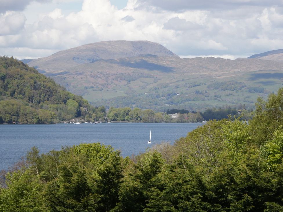 A view of mountains and a lake with a sailing boat at Owls Nook Lodge, Langdale 9, White Cross Bay near Windermere
