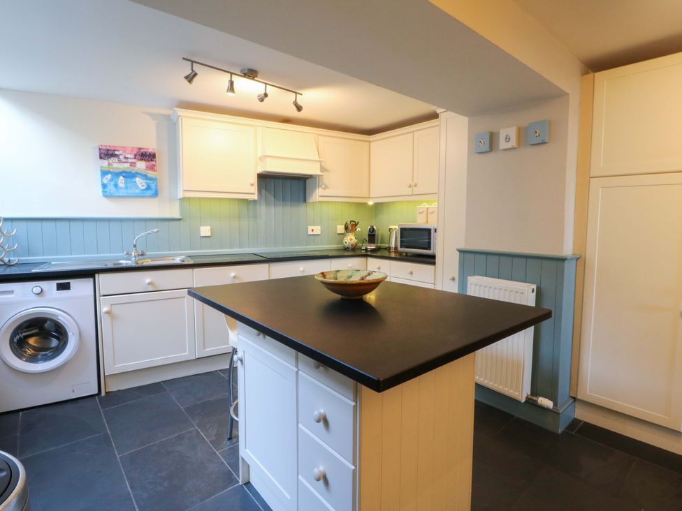 A kitchen with a sink, washing machine, and cupboards at Zenobia in New Quay