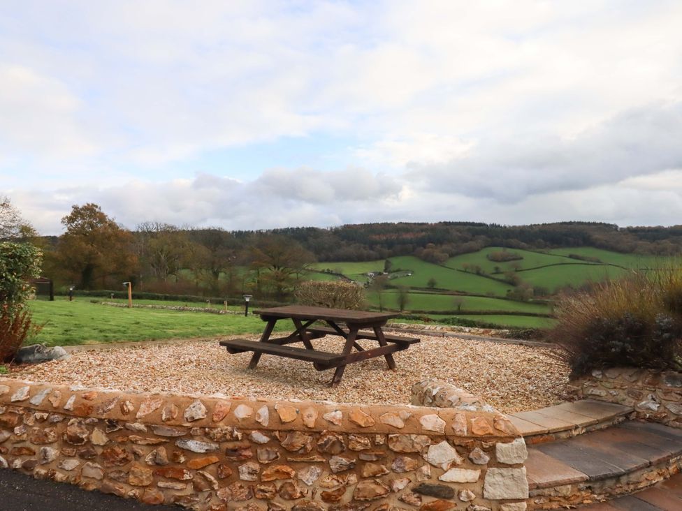 A picnic table on gravel with stone wall and hills at Higher Wadden Farm in Southleigh
