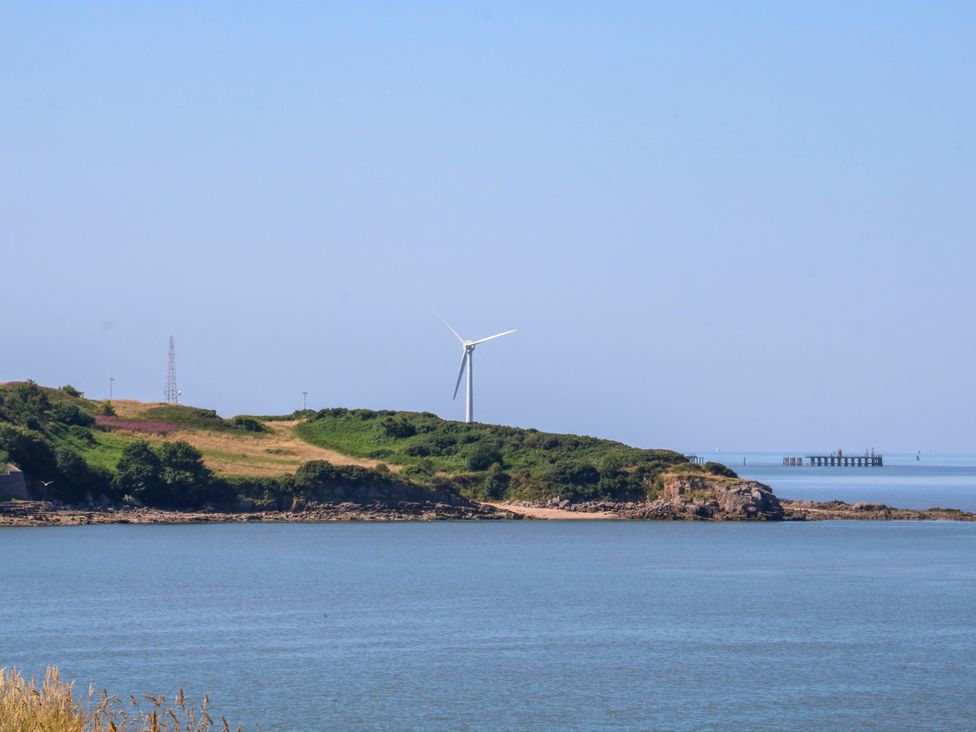 A view of a wind turbine on a hill by the water with a pier in the distance at Ferncliffe in 
