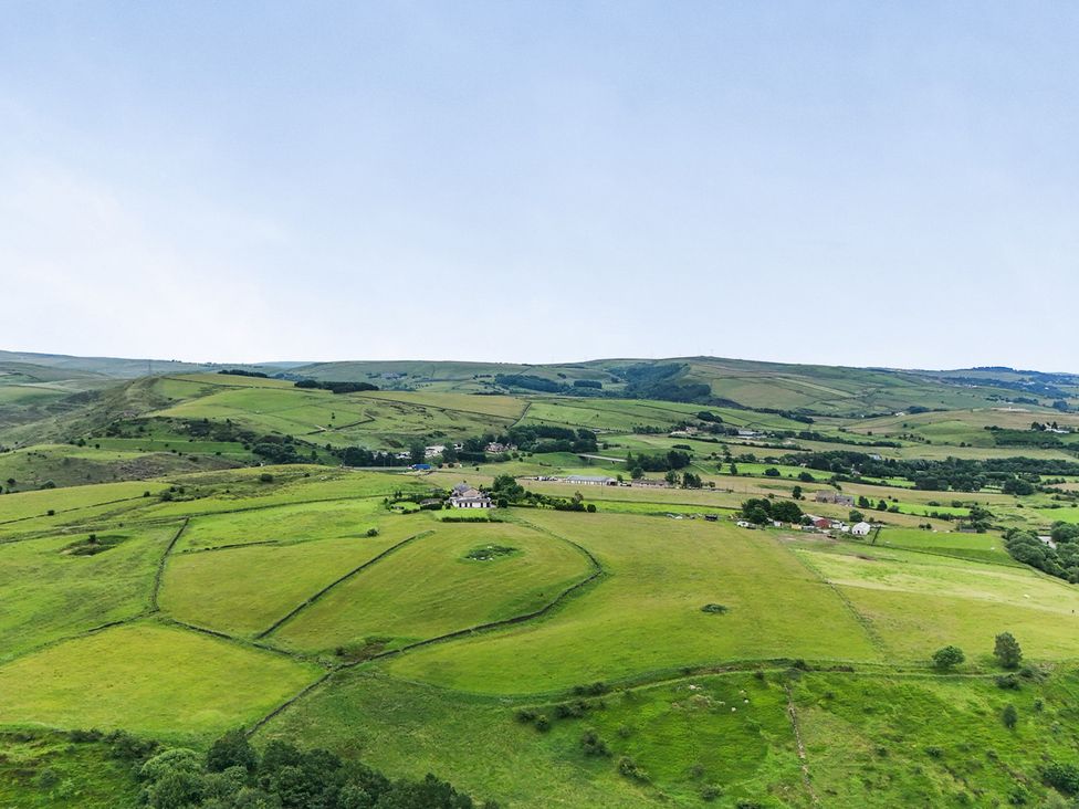 A view of green fields and hills with houses in the distance at Bib Knowl Farm in Littleborough