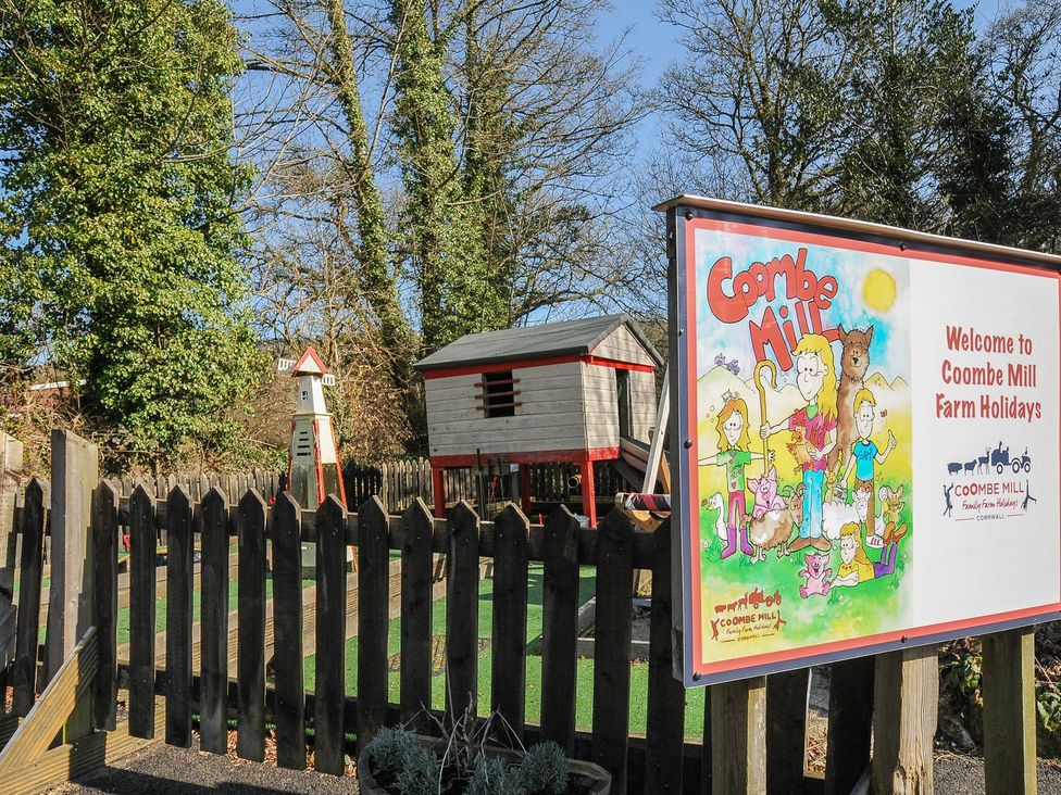 A sign welcoming to Coombe Mill Farm Holidays with a play area and trees at Coombe Mill in Cornwall