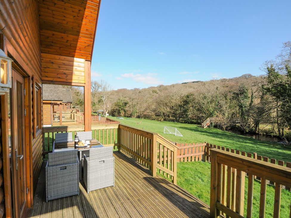 An outdoor deck with a table and chairs overlooking a grassy area at Polzeath in St Breward