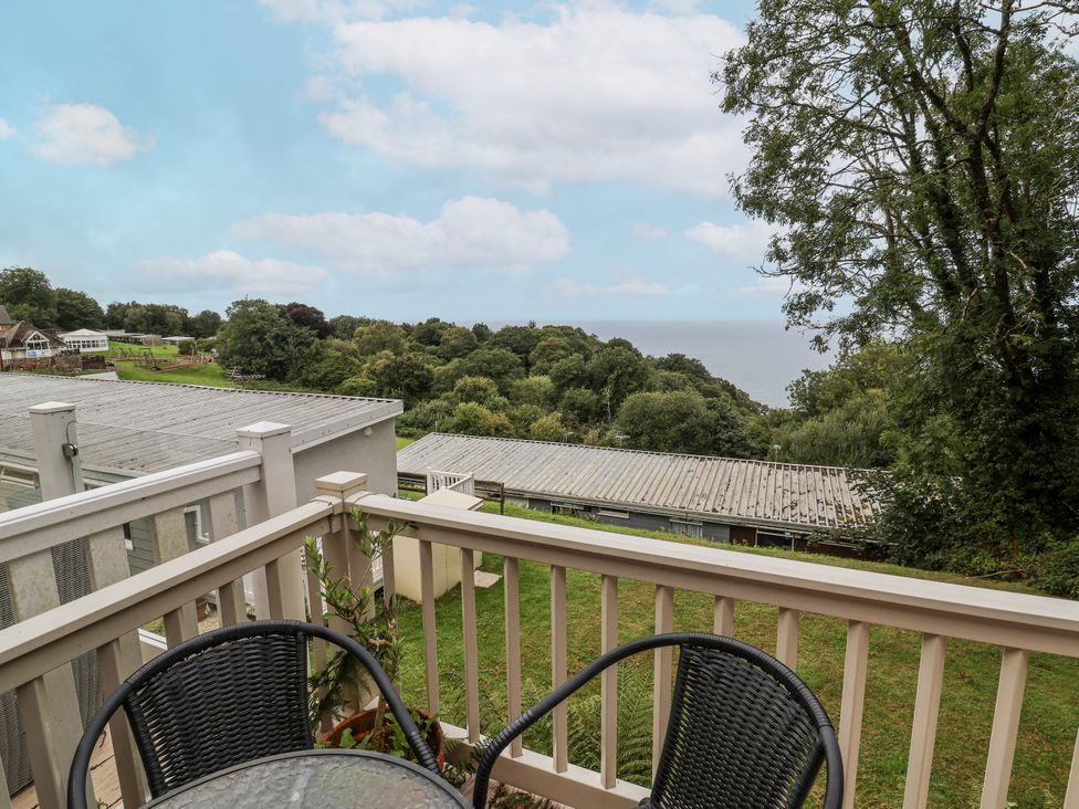 A balcony with chairs and a table overlooking trees and the sea at I C Lundy Too Bideford Bay Holiday Park near Woolfardisworthy