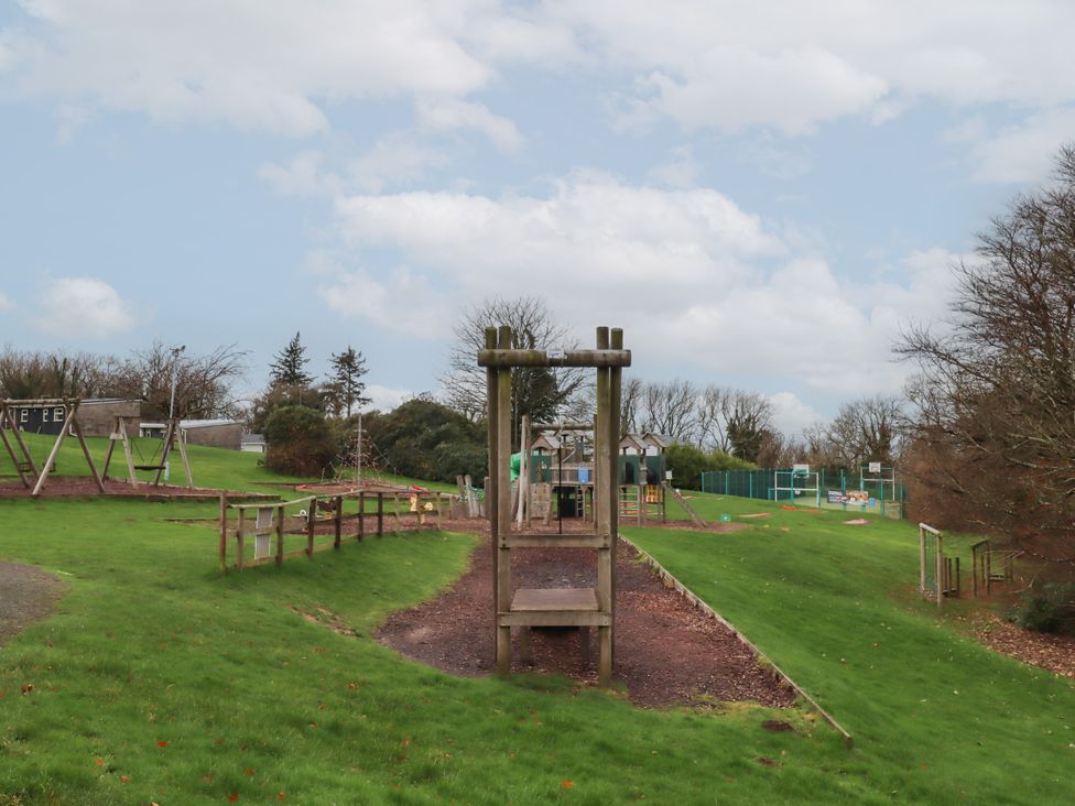 A playground area with swings and a wooden play structure at I C Lundy Too near Bideford Bay Holiday Park