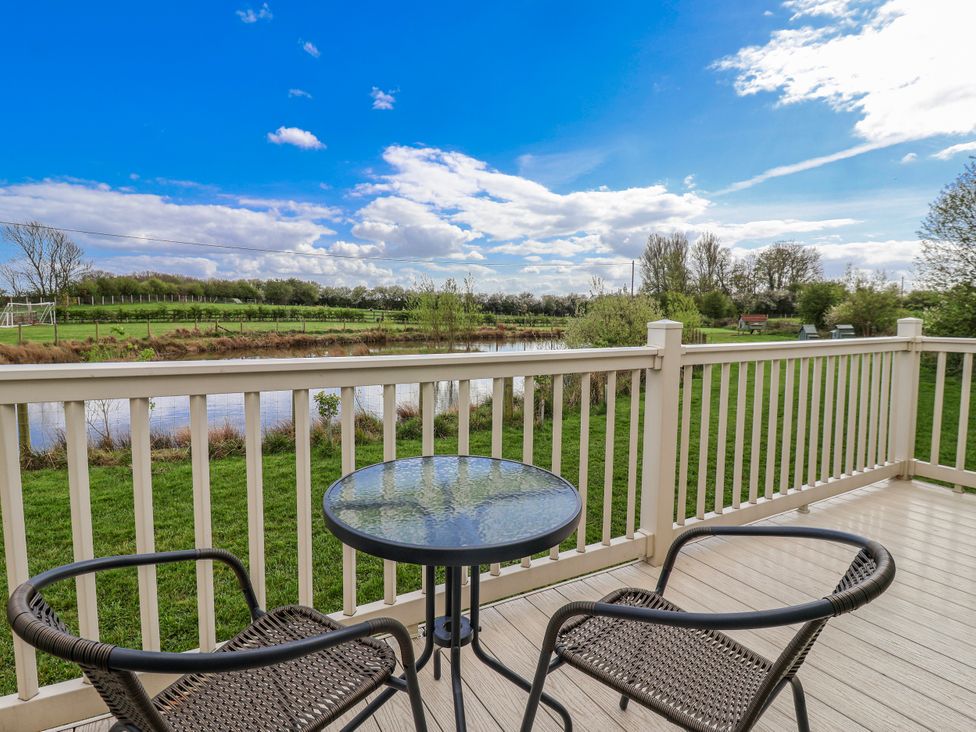A deck with a table and chairs overlooking a pond at The Dragonfly in Bewholme near Hornsea