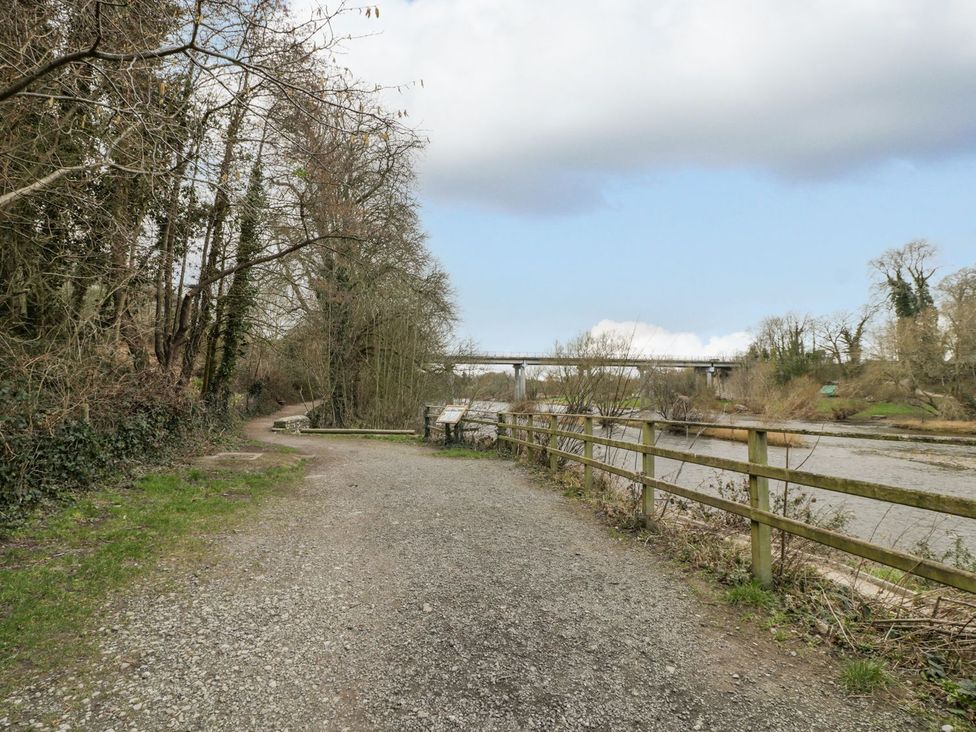 A pathway along a river with a bridge in the background at Cariad Cottage Hereford