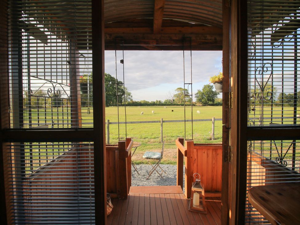 A view from a wooden structure overlooking a grassy field at Sharon's Shepherd Hut Oswestry