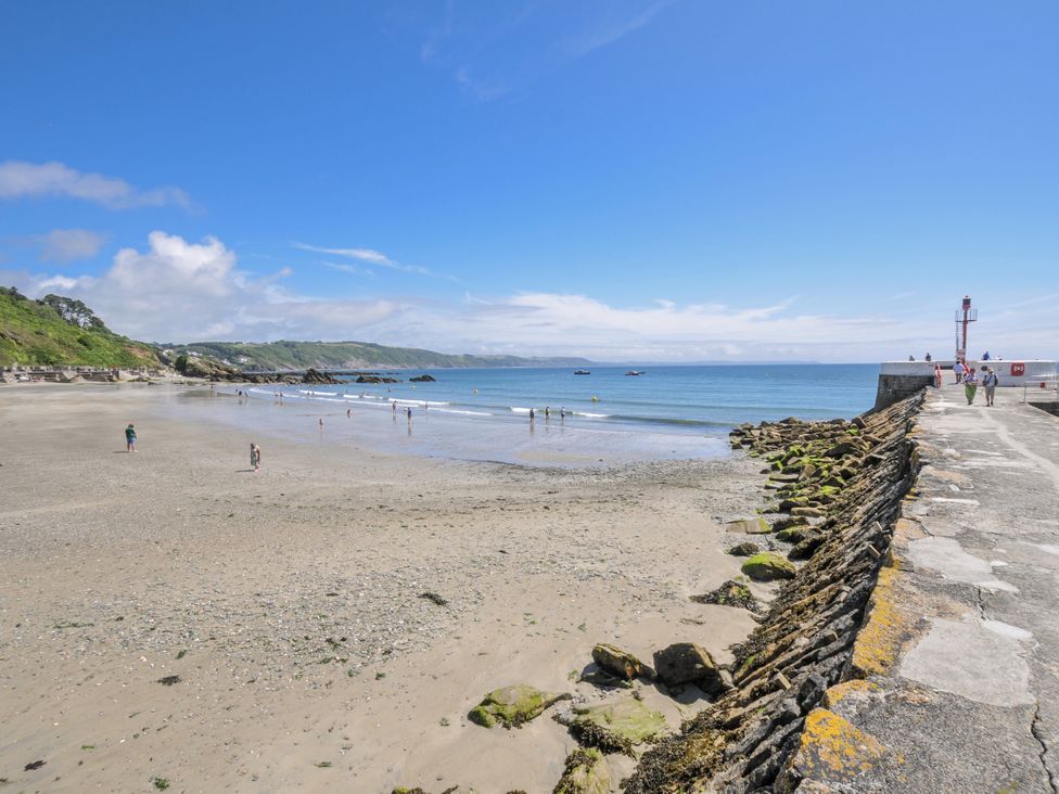 A beach with people swimming and a pier at Mayhurst in Looe