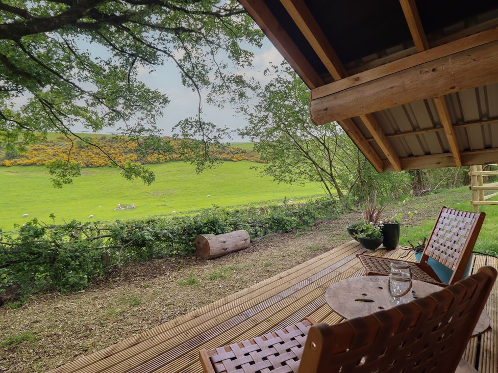 A wooden deck with chairs and a table overlooking a grassy area at Owl Valley Cabin near Bwlch-y-Ddar