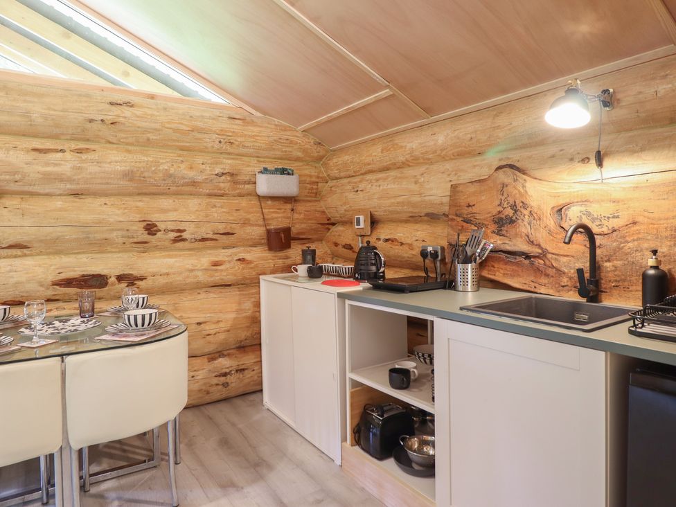 A kitchen with wooden walls, sink, and dining table at Owl Valley Cabin Bwlch-y-Ddar near Llanfyllin