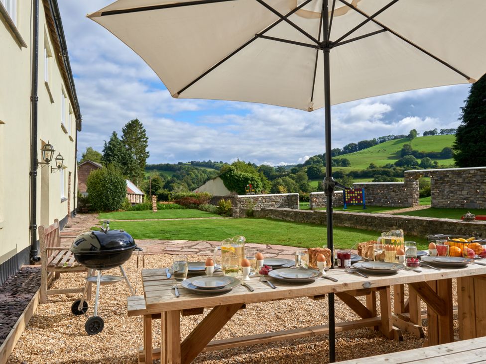 A dining table with food and drinks under an umbrella at Holwell Farmhouse in Bampton