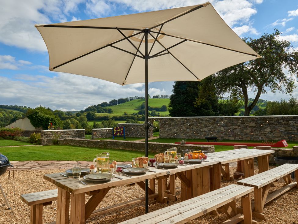 An outdoor dining area with a table under an umbrella at Holwell Farmhouse in Bampton