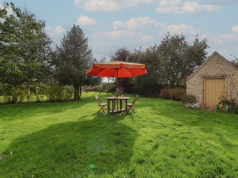 A garden with a table and chairs under an umbrella at Badminton Farm Cottage