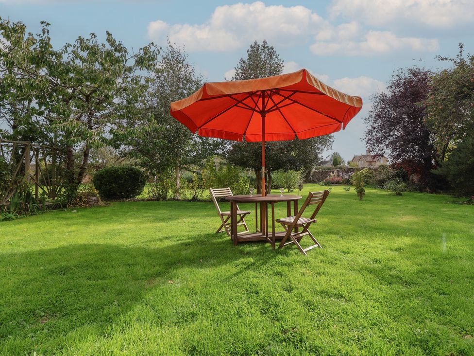 A garden with a table and chairs under an umbrella at Badminton Farm Cottage