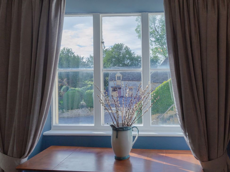 A window with curtains and a vase on a table at Badminton Farm Cottage Acton Turville
