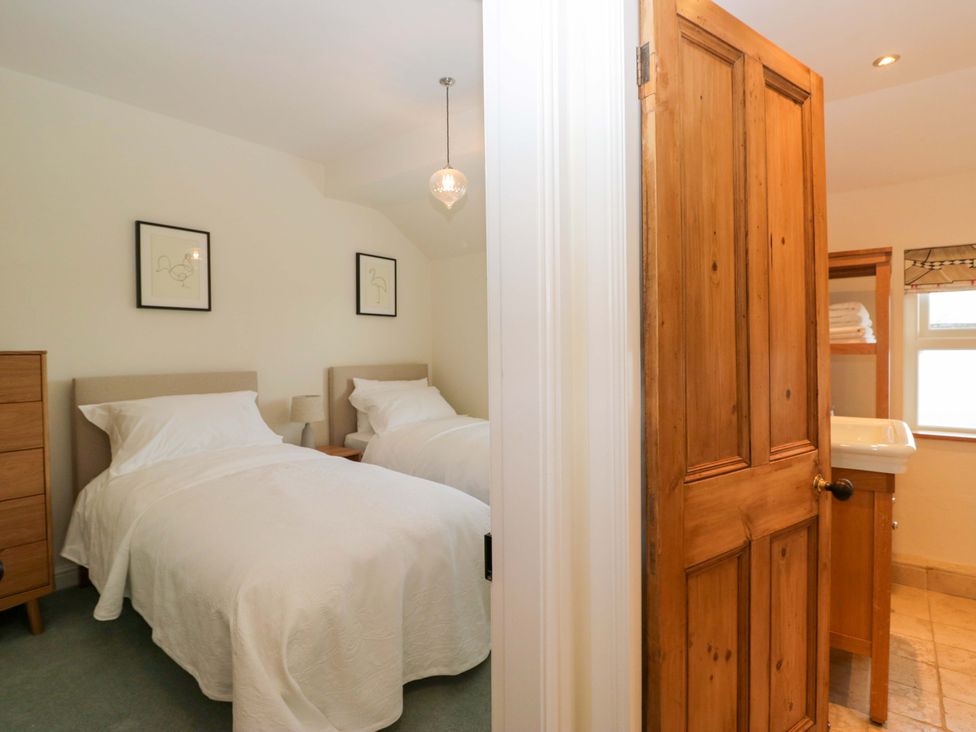 A bedroom with two beds, nightstand, and a door to a bathroom at 11 Tram Lane in Kirkby Lonsdale