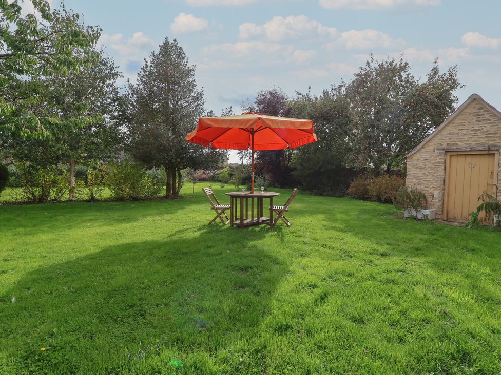 A garden with a table and chairs under an umbrella at The Old Dairy Acton Turville near Nettleton