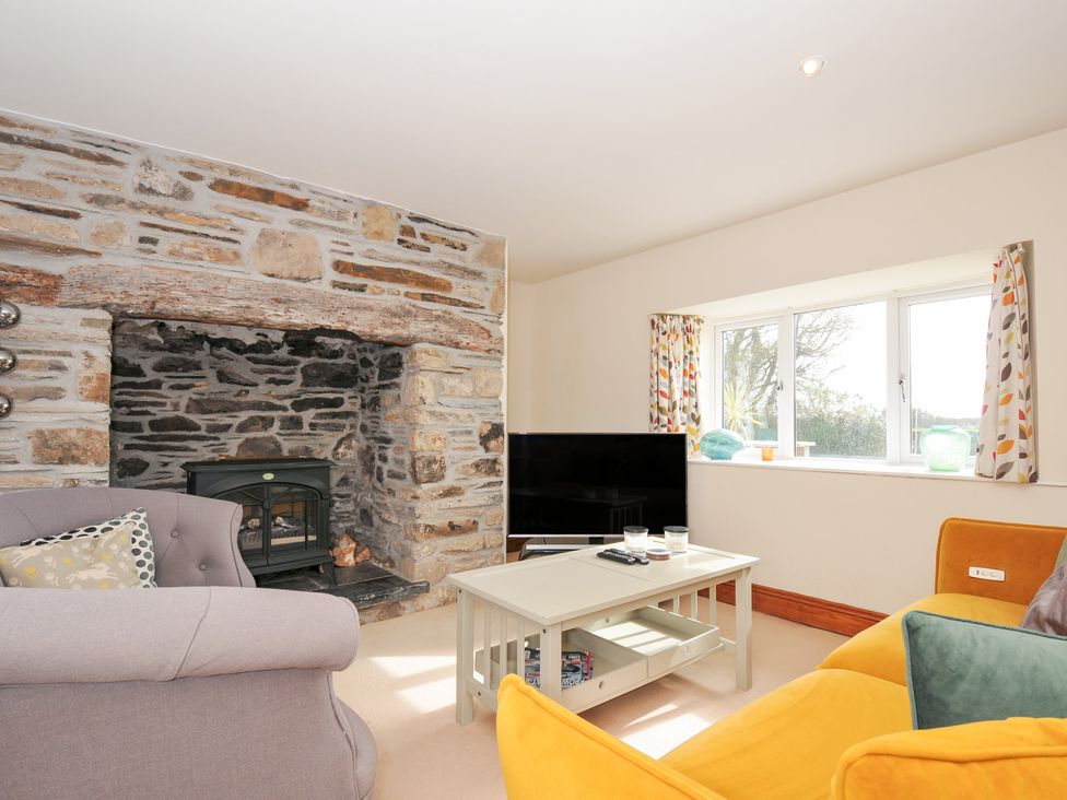 A living room with a fireplace and a television at Rosewin Farmhouse near St Minver