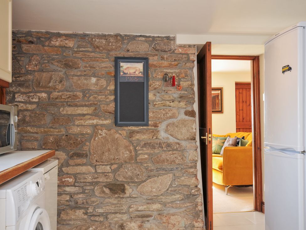 A kitchen with a stone wall and a doorway leading to a living area at Rosewin Farmhouse near St Minver