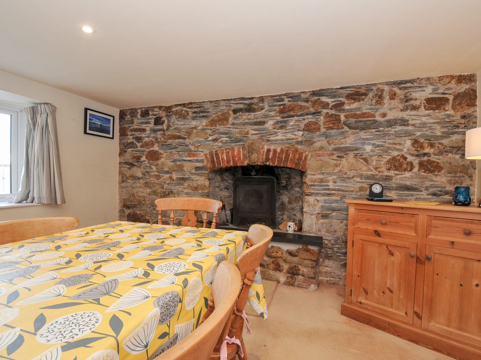 A dining room with a stone fireplace and wooden table at Rosewin Farmhouse near St Minver