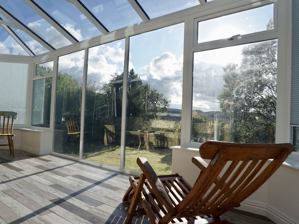 A conservatory with wooden chairs and glass panels at The Peak View Holmfirth