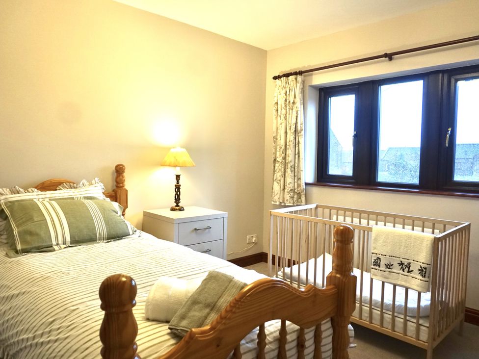 A bedroom with a bed, lamp, side table, and crib at The Peak View Holmfirth