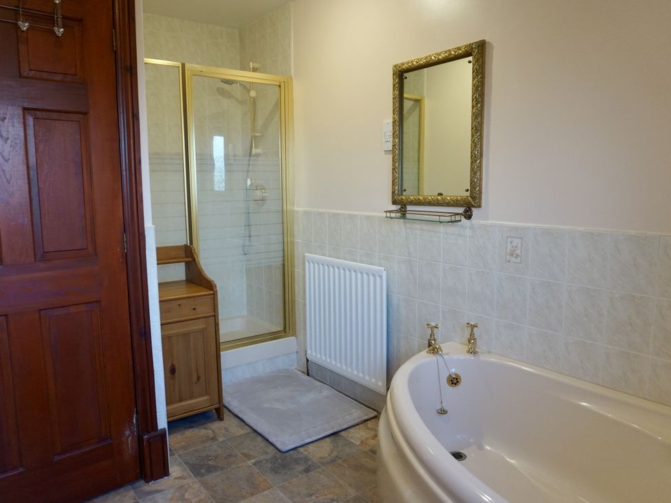 A bathroom featuring a bathtub, shower, mirror, and wooden cabinet at The Peak View Holmfirth