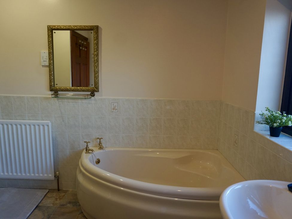 A bathroom with a bathtub, mirror, radiator, and plant at The Peak View Holmfirth