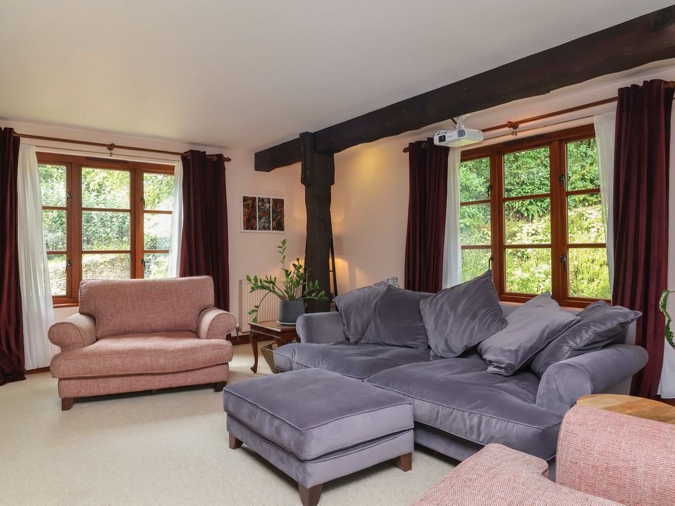 A living room with a sofa, chair, and windows at Hedgerose in Goodleigh near Barnstaple
