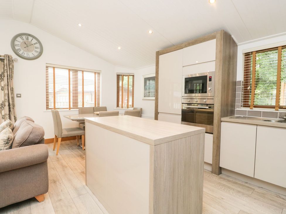 A kitchen with a table, chairs, and a wall clock at Easedale Lodge, Waterside Wood 2, White Cross Bay near Windermere