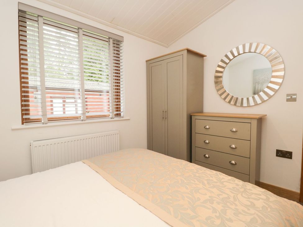 A bedroom with a bed, wardrobe, mirror, and chest of drawers at Easedale Lodge, Waterside Wood 2, White Cross Bay near Windermere