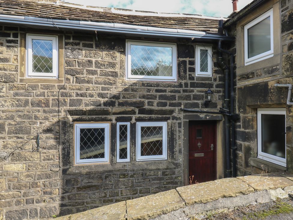 An exterior view of a stone building with windows and a door at 11 Hollin Well Cottage, Sowerby Bridge