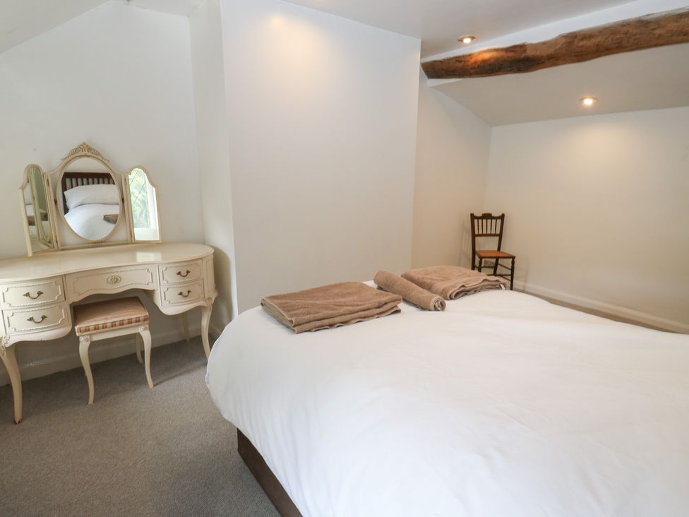 A bedroom with a bed, vanity table with a mirror, and a chair at 11 Hollin Well Cottage, Sowerby Bridge