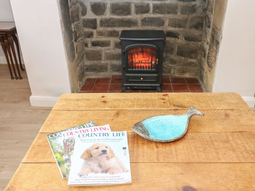 A living room with a fireplace and magazines on a wooden table at 11 Hollin Well Cottage in Sowerby Bridge