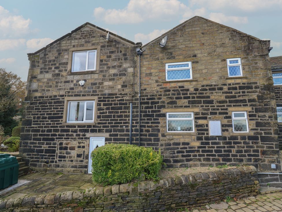 A stone building with windows and a door surrounded by a garden at 11 Hollin Well Cottage in Sowerby Bridge
