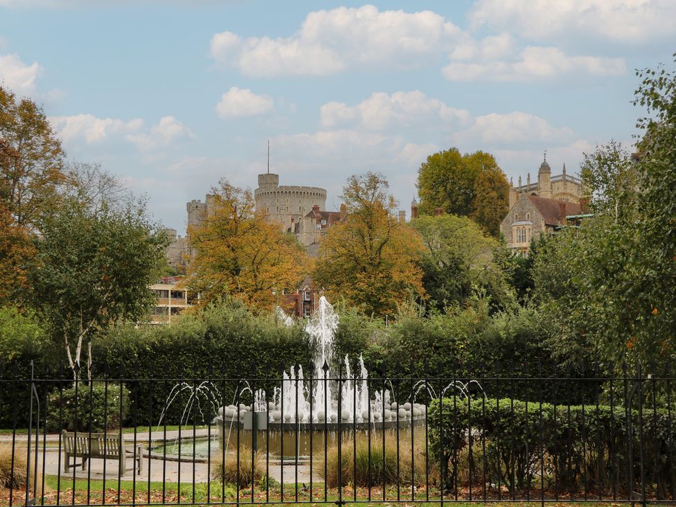 A fountain with benches and trees in front of a castle at Castle View in Windsor, Berkshire