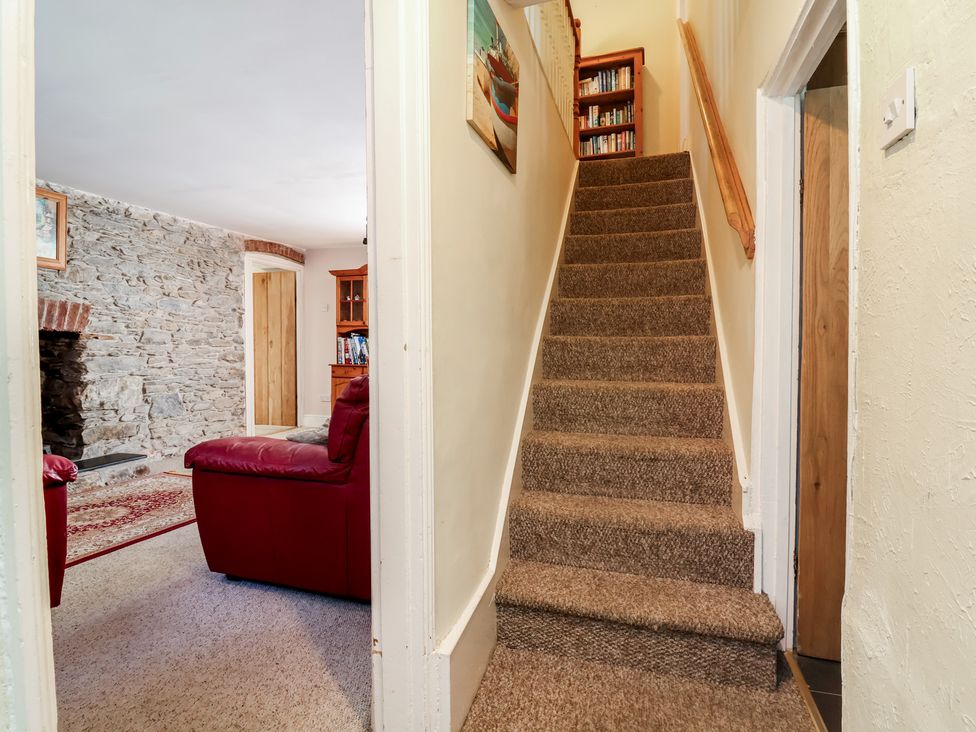 A hallway with a staircase and a red sofa at Honey Cottage in Ilfracombe