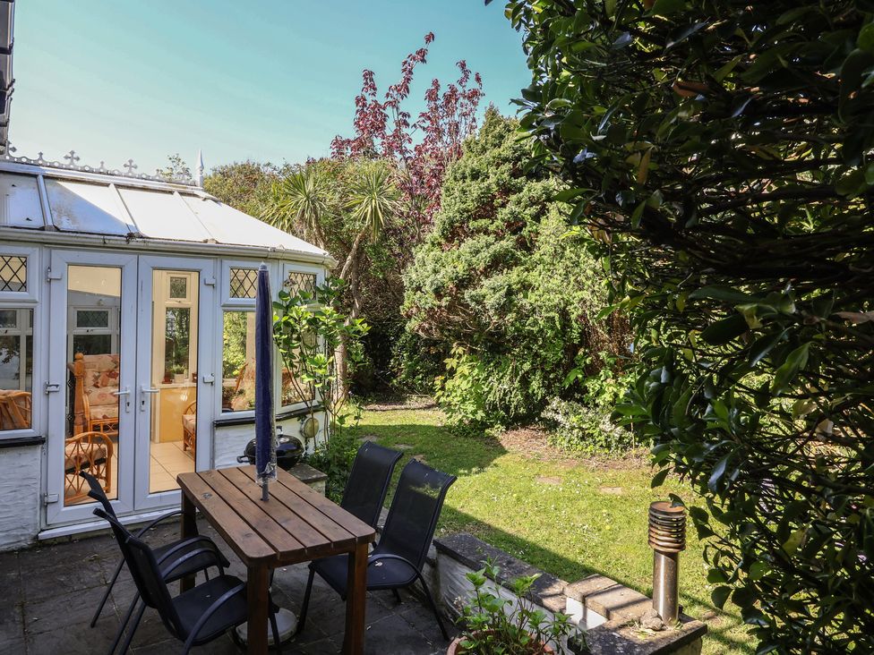 A garden with a table and chairs near a conservatory at Honey Cottage Ilfracombe