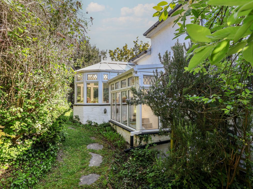 A garden with a conservatory and pathway at Honey Cottage in Ilfracombe