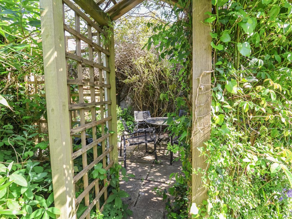 A garden area with a table and chairs under a trellis at Honey Cottage in Ilfracombe